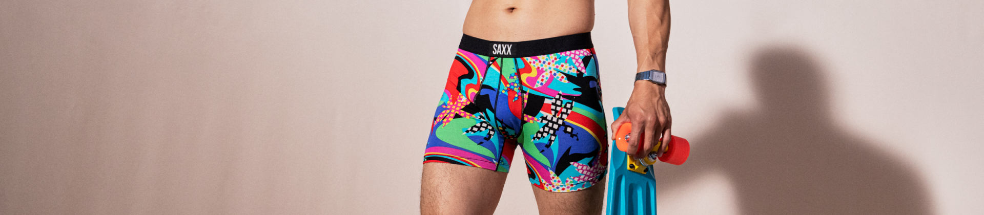 Man standing in very colorful Vibe underwear holding skateboard