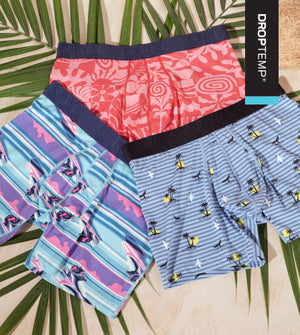 3 pairs of SAXX boxer briefs in colorful summery prints laid out over a neutral backdrop over a green palm leaf. 