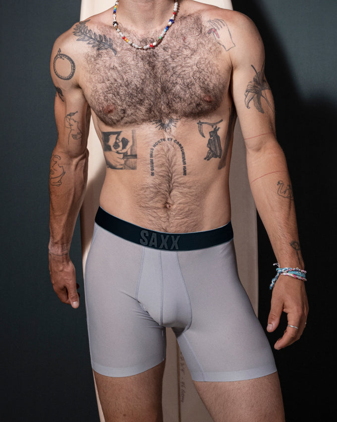 An image of a man's body from the next to mid thigh. He is stood against a surfboard wearing grey boxer briefs.