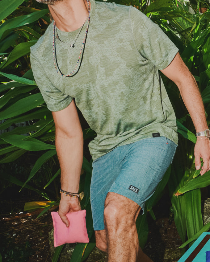 An image of a man from the neck to the ankle. He is holding a bean bag and in a pose suggesting he is about to throw it.