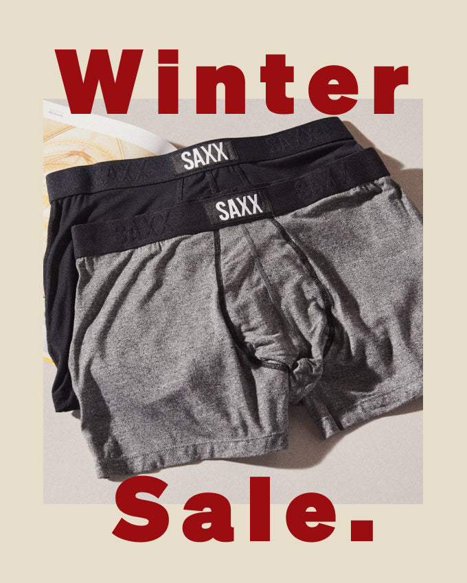 Two pairs of black and grey SAXX Trunks laid out over a neutral backdrop. Reads ‘Winter Sale.’