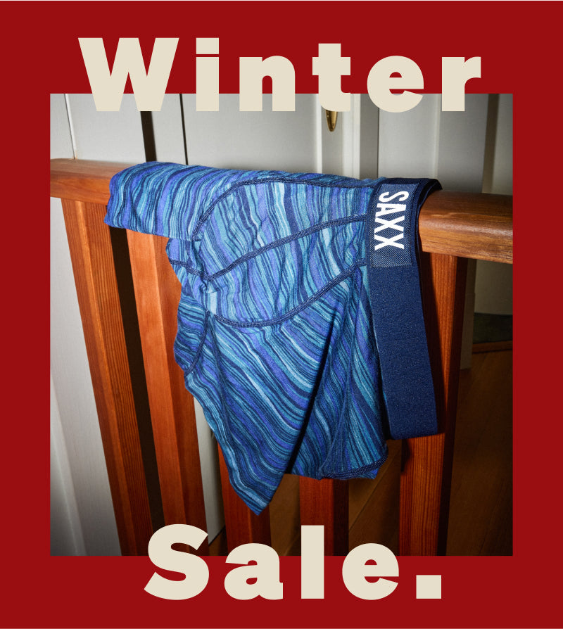 A pair of blue and green striped SAXX Boxer Briefs hanging over a wooden railing. Text reads ‘Winter Sale.’