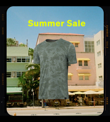 A snapshot of a street scene with a pink building with yellow awnings and a patio with yellow umbrellas out front, with a green camo-patterned SAXX crew neck tee shirt overlaying the image along with the text "Summer Sale".