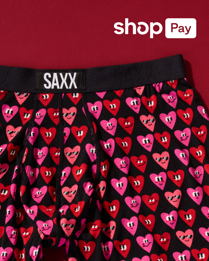 Black Valentine’s themed SAXX Boxer Briefs with pink and red smiling hearts pattern over red background. Text reads ‘ShopPay.