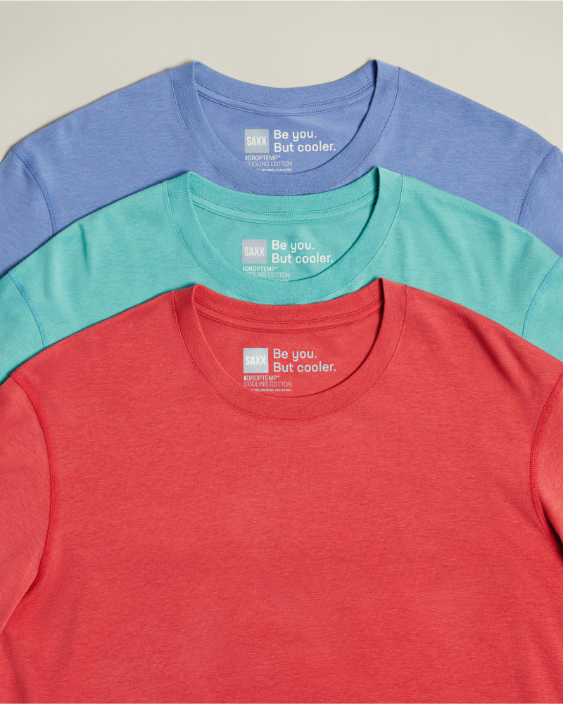 Three SAXX DropTemp® Cooling tops in red, green, and blue, laid out flat over neutral background.