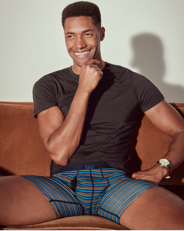 A man sitting on a leather seat wearing striped boxer briefs and a black t-shirt. 