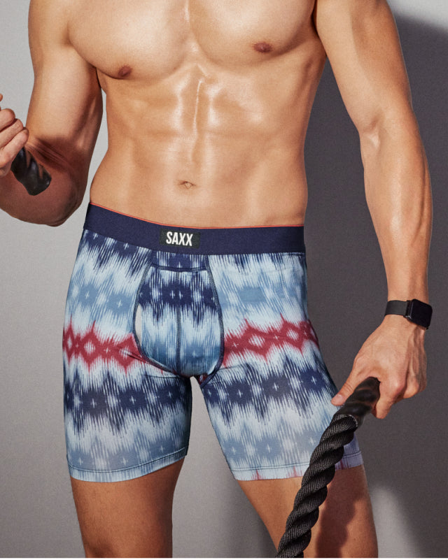 A close up of a man’s torso and patterned underwear. He is holding a whip.  