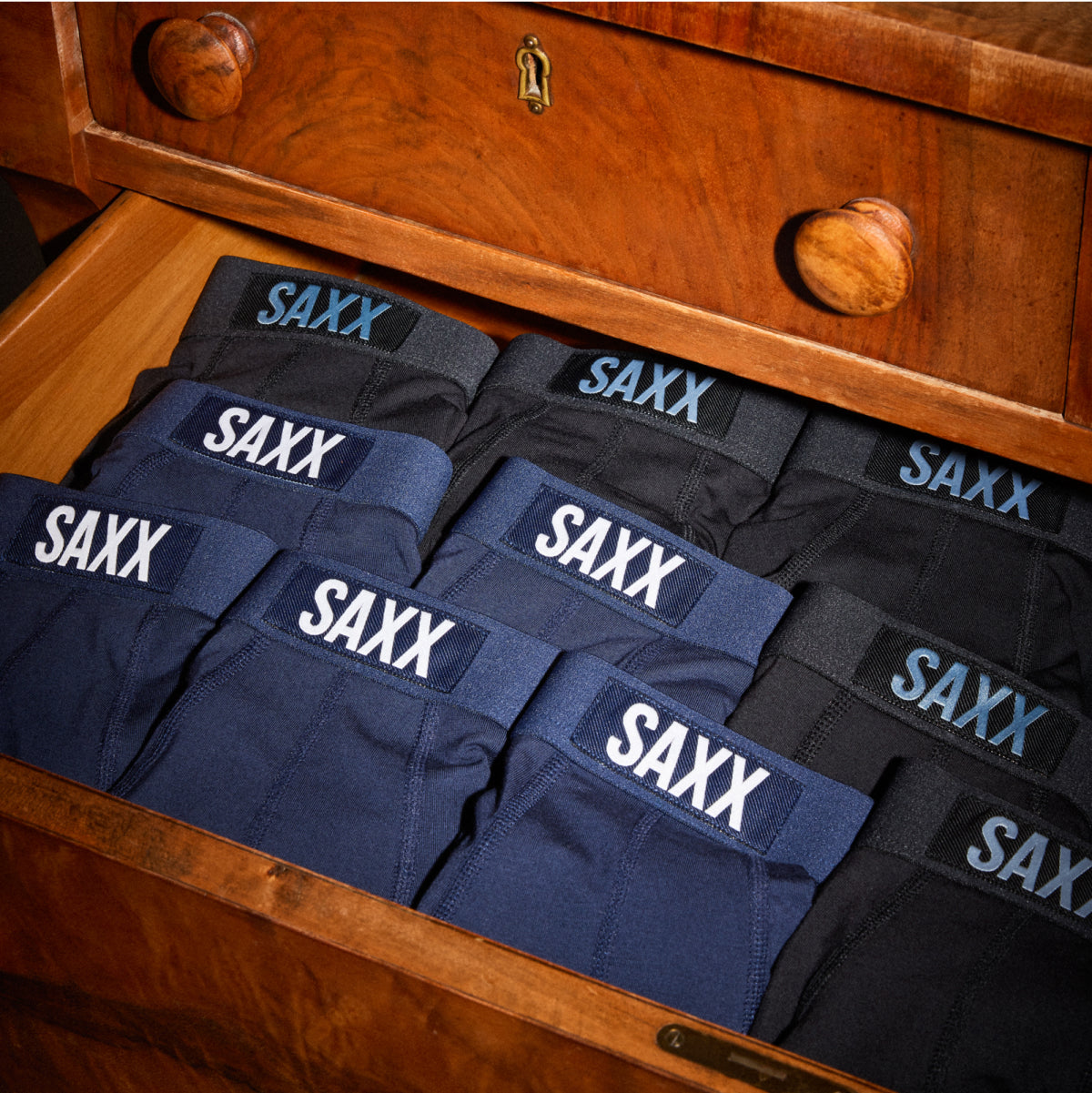 A drawer full of neatly folded underwear in navy and black colors with their waistbands clearly visible. 