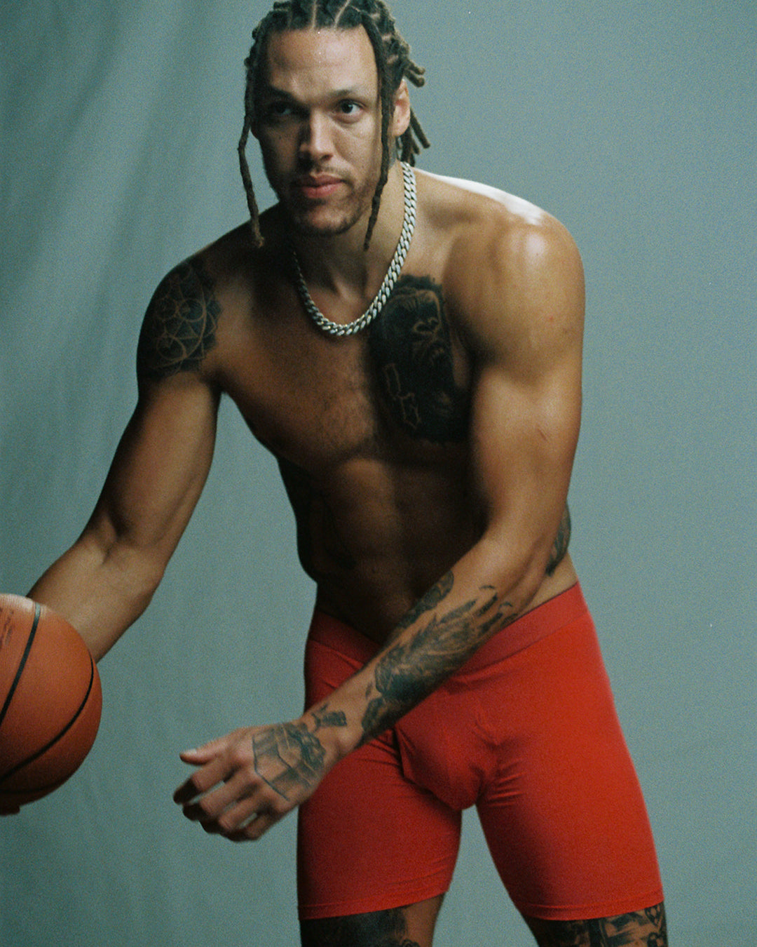 A man wearing red boxer briefs leaning towards us. He is holding a basketball.